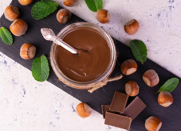 Pâte à tartiner au chocolat aux noisettes dans un bocal sur une ardoise noire Mise à plat