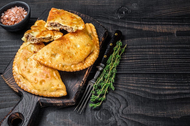 Pâté à la viande Cheburek aux herbes. Fond en bois noir. Vue de dessus. Espace de copie.