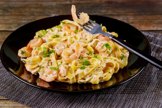 Pâtes Alfredo fettuccine aux crevettes sur plaque noire.