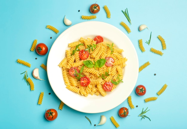 Pâtes alimentaires sur fond bleu. Pâtes fusilli italiennes aux tomates, herbes et basilic sur une assiette blanche.