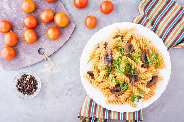 Pâtes appétissantes avec champignons sautés, tomates et herbes fraîches sur une assiette, vue de dessus