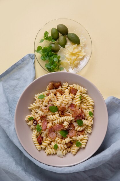 pâtes au bacon sur une surface jaune. Olives vertes et basilic frais. Surface verticale