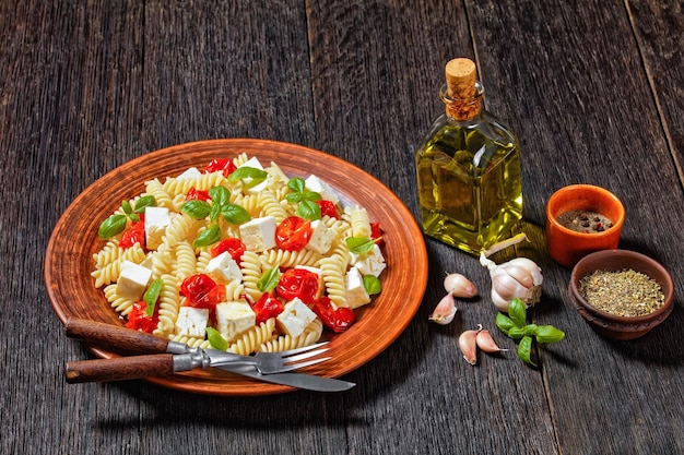 Pâtes au fromage feta au four avec tomates cerises et basilic dans une plaque d'argile rustique sur une table en bois, cuisine italienne