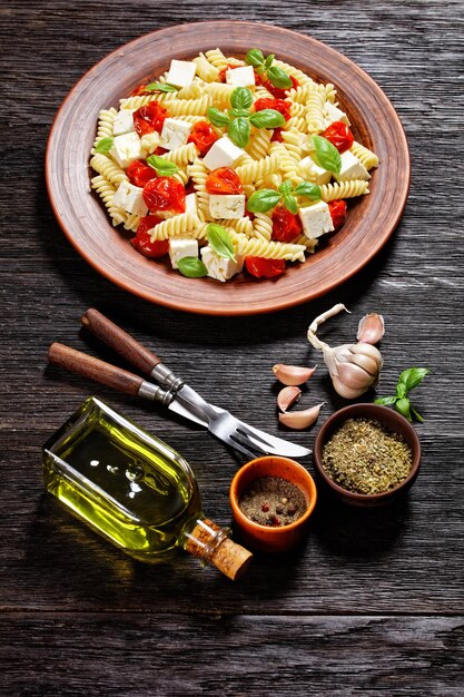 Pâtes au fromage feta au four avec tomates cerises et basilic dans une plaque d'argile rustique sur une table en bois, vue verticale, cuisine italienne