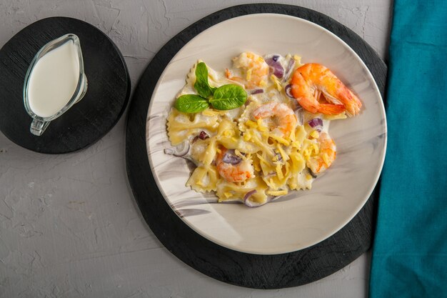 Pâtes aux crevettes dans une sauce crémeuse sur une plaque grise sur un fond de béton à côté d'une serviette bleue et d'un pichet de crème.