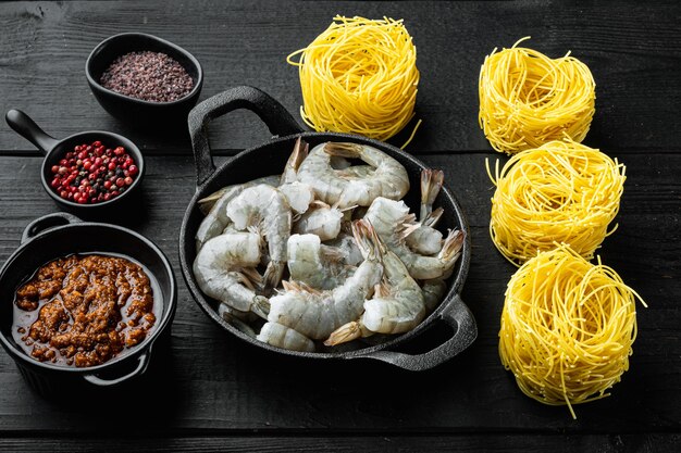 Pâtes aux crevettes, tomates et sauce pesto, ensemble d'ingrédients sur table en bois noir