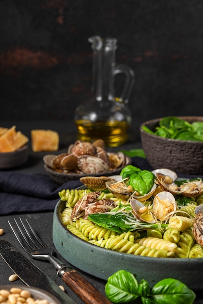 Pâtes aux fruits de mer avec palourdes, fusilli, épinards, parmesan, pignons et basilic dans une assiette sur une surface noire