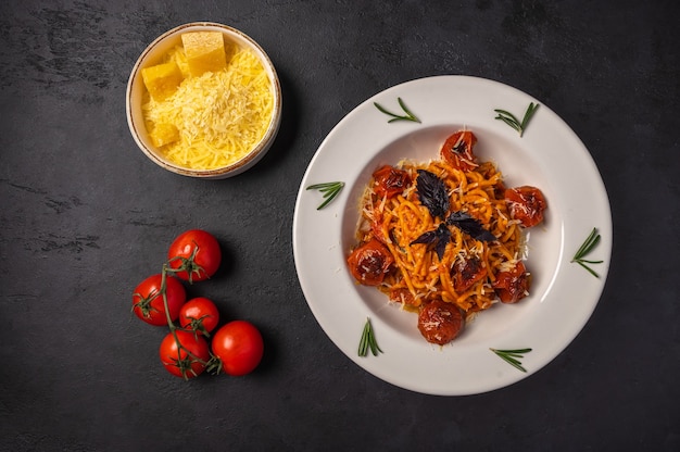 Pâtes aux tomates au four, parmesan râpé et sauce pesto dans des bols en céramique sur fond de graphite foncé, vue du dessus, espace copie