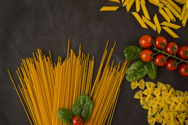 Pâtes aux tomates cerises et épinards sur fond noir à plat