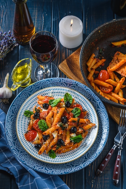 Pâtes aux tomates cerises, mozzarella et olives d'épinards, vin et huile sur une table en bois. Style rustique.