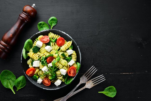 Pâtes aux tomates épinards et fromage feta Dans une assiette noire sur un fond en bois Vue de dessus Espace libre pour votre texte Mise à plat