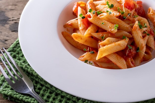 Pâtes aux tomates en sauce rouge sur une plaque blanche sur fond de bois