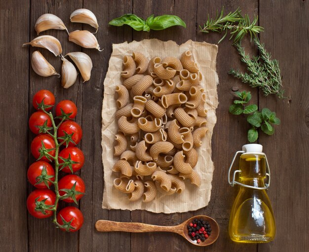 Pâtes de blé entier, légumes, herbes et huile d'olive sur la vue de dessus en bois