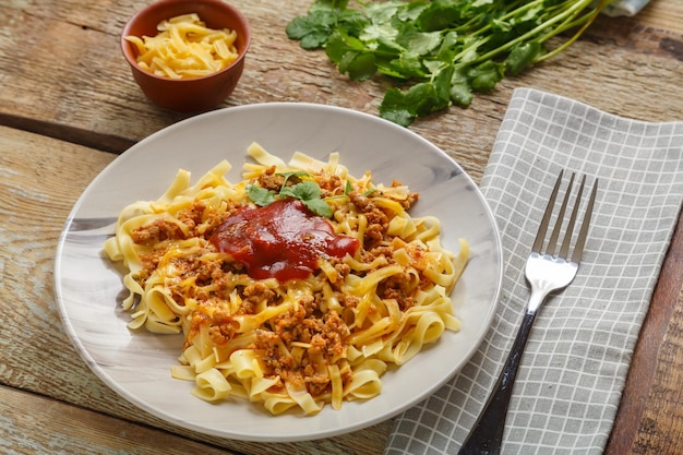 Pâtes bolognaise garnies d'herbes et de fromage dans une assiette sur une table en bois à côté d'une fourchette