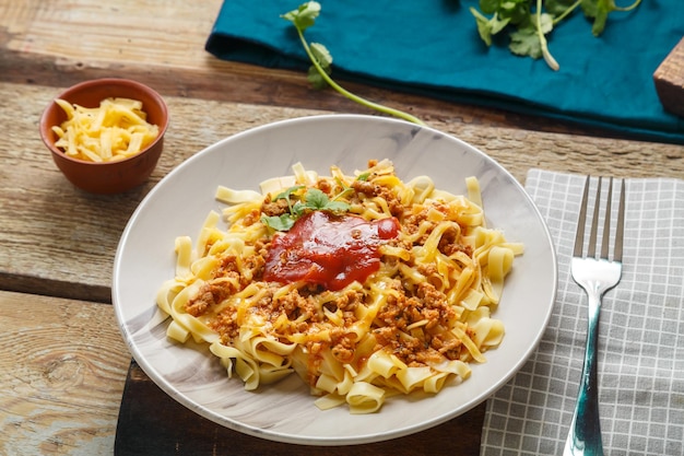 Pâtes bolognaise garnies de légumes verts et de fromage dans une assiette sur une table en bois à côté d'une fourchette