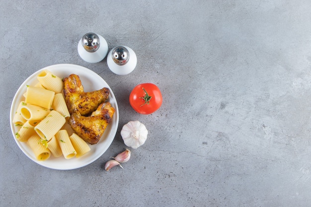 Pâtes calamarata avec ailes de poulet frites sur plaque blanche.