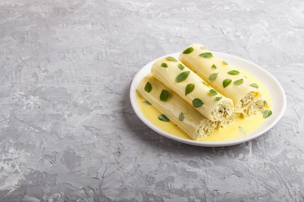 Pâtes cannelloni avec sauce aux œufs, fromage à la crème et feuilles d'origan sur fond de béton gris. vue de côté
