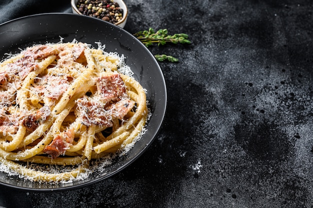 Pâtes carbonara, bucatini à la pancetta, œuf, parmesan et sauce à la crème. Fond noir. Vue de dessus. Espace copie