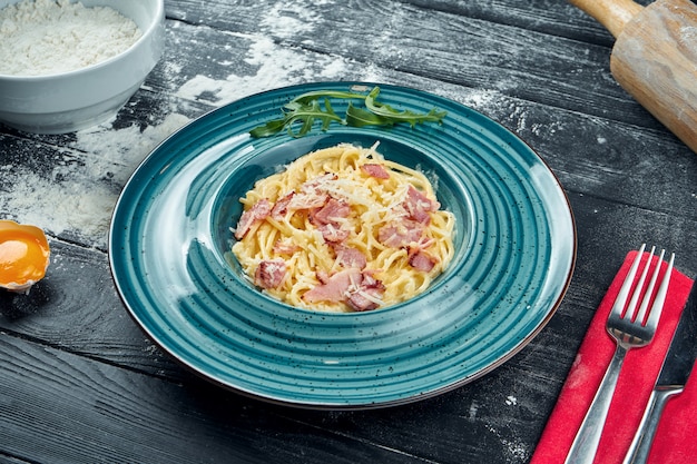 Pâtes carbonara maison appétissantes avec bacon, sauce à la crème et parmesan dans une assiette bleue. Gros plan, vue de dessus. Spaghetti italien, photo pour la recette