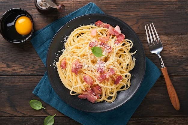 Pâtes à la carbonara Spaghetti aux œufs de pancetta, fromage parmesan et sauce à la crème sur fond de table en bois noir foncé Cuisine et plat traditionnels italiens Pâtes alla carbonara Vue de dessus