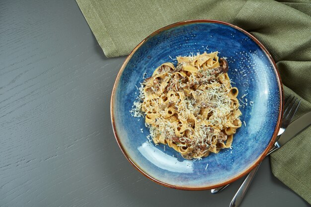 Pâtes classiques aux champignons sauvages, sauce à la crème et parmesan dans une assiette bleue sur une table en bois. Vue de dessus, mise à plat, espace copie