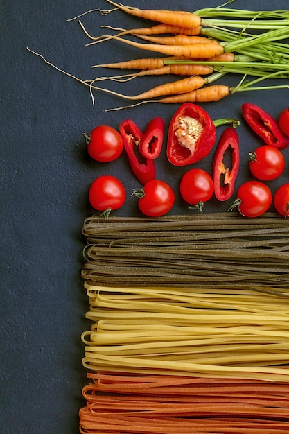 Pâtes colorées faites maison avec des ingrédients naturels sur une table en béton noir Nouilles aux tomates carottes épinards