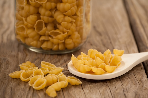 Pâtes Conchiglie débordant de pot et cuillère sur table en bois