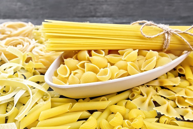 Pâtes coquillages et spaghettis dans un bol, pipe rigate, tagliatelles, fusilli, penne, farfalle, conquilla, trenette, rotini, pappardelle sur fond de planche de bois