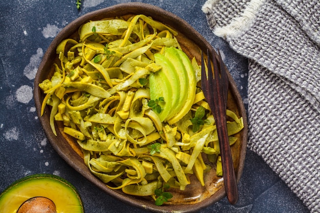 Pâtes de courgettes au pesto et avocat dans un plat noir. Nourriture végétalienne saine.