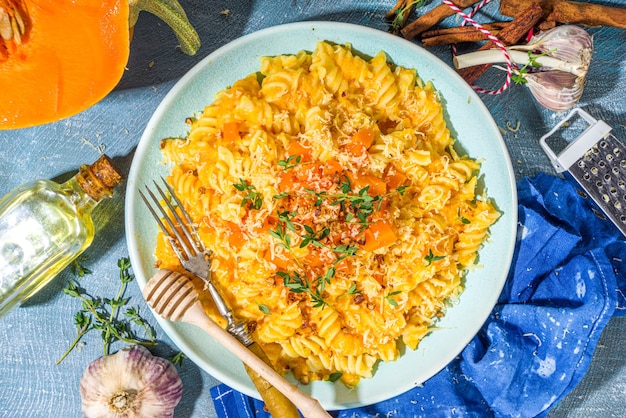 Pâtes crémeuses à la citrouille végétalienne au fromage, fusilli avec sauce à la courge citrouille, fromage et thym, sur fond de table bleu en béton, espace de copie