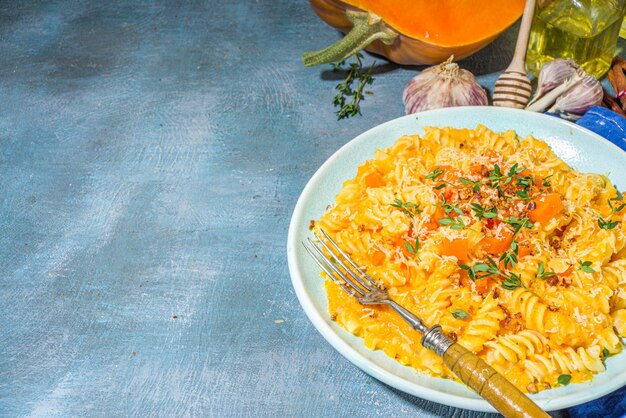 Pâtes crémeuses à la citrouille végétalienne au fromage, fusilli avec sauce à la courge citrouille, fromage et thym, sur fond de table bleu en béton, espace de copie