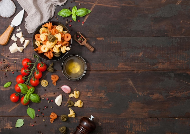 Pâtes crues fraîches trottole tricolore dans un bol noir avec tomates cerises et basilic ail et huile avec parmesan sur fond bois Espace pour le texte