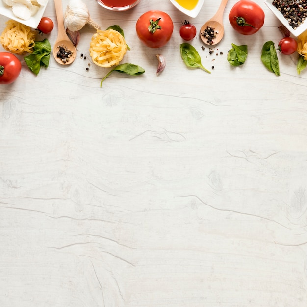 Photo pâtes crues et ses ingrédients rangés en rangées sur une table en bois blanche