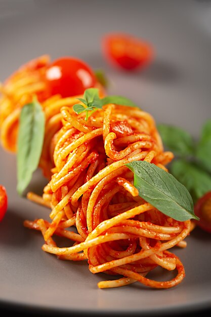 Pâtes cuites dans un restaurant à la sauce tomate avec tomates cerises et basilic et servies sur une assiette grise