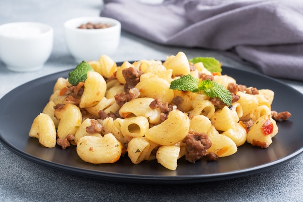 Pâtes à l'étouffée avec boeuf haché et légumes, macaronis à la marine sur une assiette. fond de béton gris.