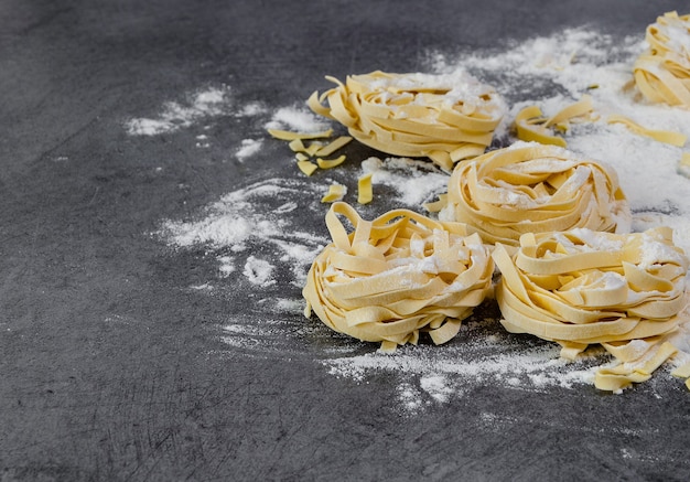 Les pâtes faites à la main des tagliatelles crues avec de la farine sur une table sombre