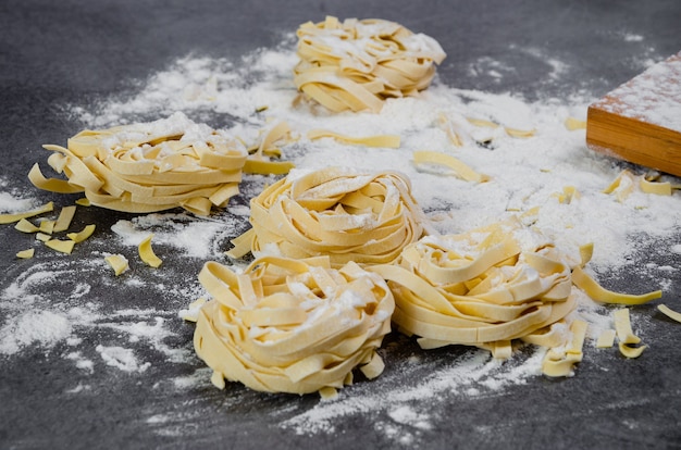 Les pâtes faites à la main des tagliatelles crues avec de la farine sur une table sombre