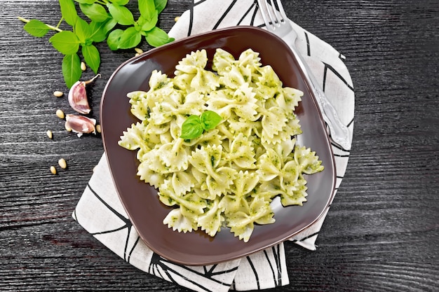 pâtes farfalle au pesto, basilic dans une assiette sur une serviette sur fond de planche de bois foncé d'en haut