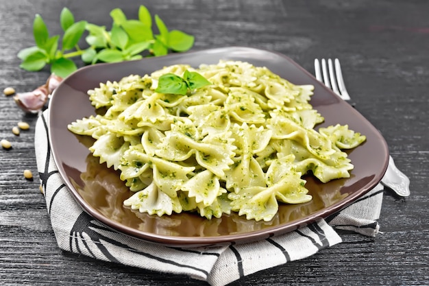 Pâtes Farfalle au pesto, basilic dans une assiette sur une serviette sur fond de planche de bois