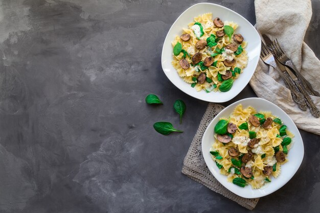 Pâtes farfalle maison fraîches aux champignons et épinards sur fond de béton