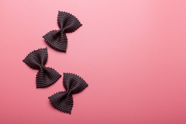 Pâtes farfalle noires sur fond rose, fond à gauche