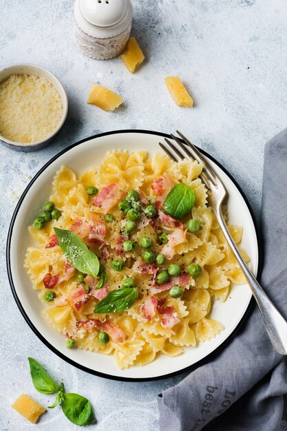 Pâtes fettuccine au bacon et pois verts et fromage parmesan en plaque légère sur la vieille surface de béton gris