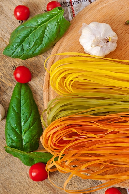 Pâtes fettuccine colorées et ingrédients de cuisine sur table en bois