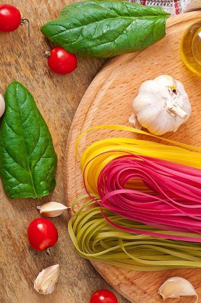 Pâtes fettuccine colorées et ingrédients de cuisine sur table en bois