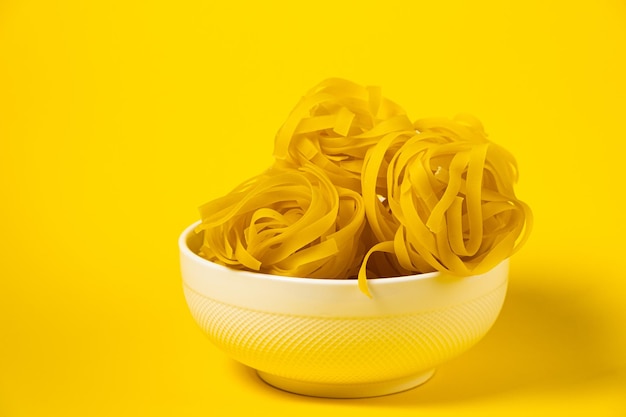 Pâtes fettuccine crues dans une assiette isolée sur fond jaune