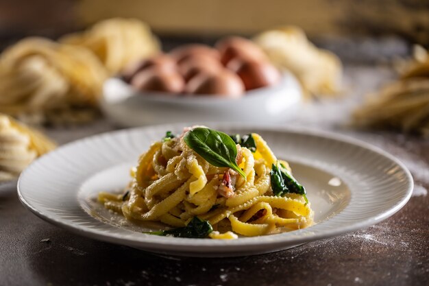 Pâtes fettuccine fraîches cuites servies sur une assiette avec épinards et bacon.