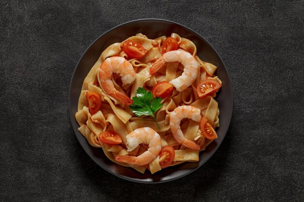 Pâtes fettuccine à la sauce tomate crevettes et tomates sur plaque grise vue de dessus fond sombre avec espace pour copier du texte