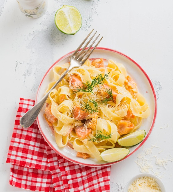 Pâtes fettucine au saumon et parmesan en sauce crémeuse dans une assiette en céramique sur fond de béton clair ancien. Vue de dessus.