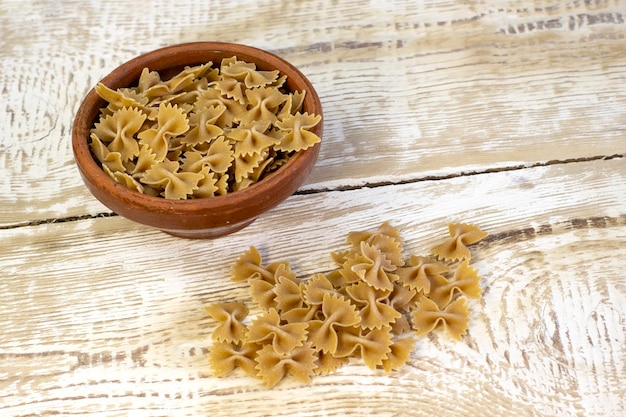 Les pâtes foncées à grains entiers s'inclinent sur une plaque brune sur un fond clair en bois rugueux avec une mise au point sélectionnée