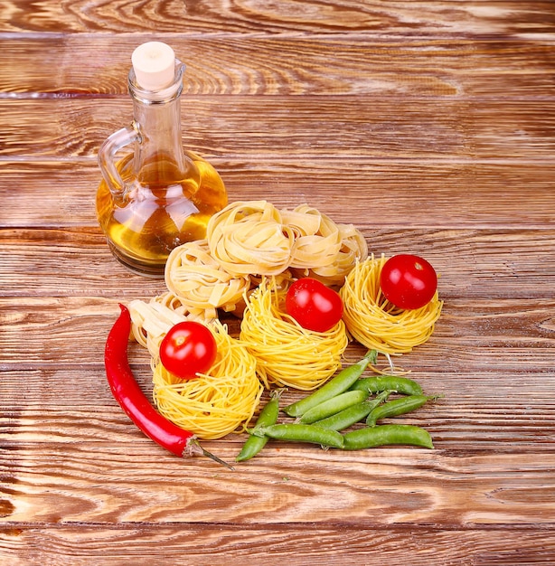 Pâtes sur le fond en bois avec tomate, laitue poivron, huile d'olive et poivre